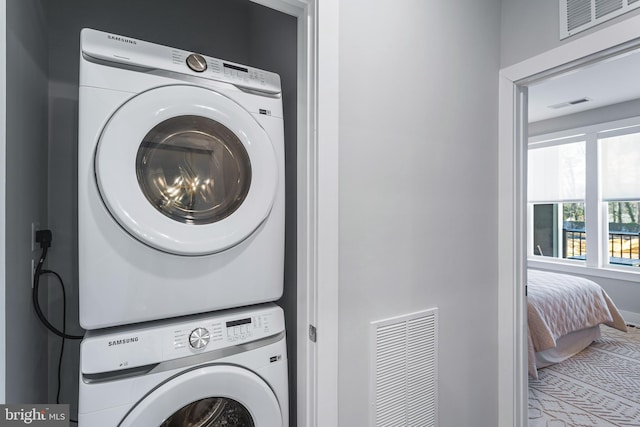 clothes washing area featuring stacked washer and clothes dryer, visible vents, and laundry area