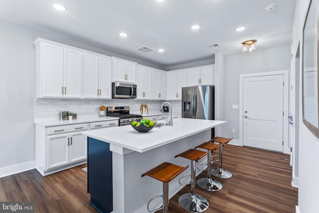 kitchen with stainless steel appliances, dark wood-style flooring, visible vents, a kitchen breakfast bar, and backsplash