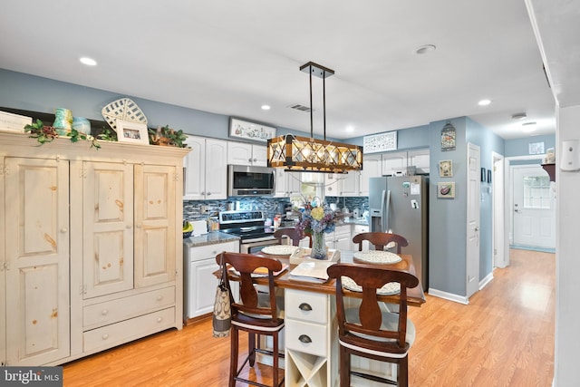 kitchen with stainless steel appliances, visible vents, hanging light fixtures, decorative backsplash, and light wood-style floors