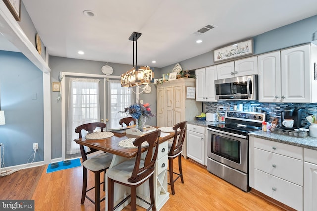 kitchen with tasteful backsplash, appliances with stainless steel finishes, visible vents, and white cabinetry