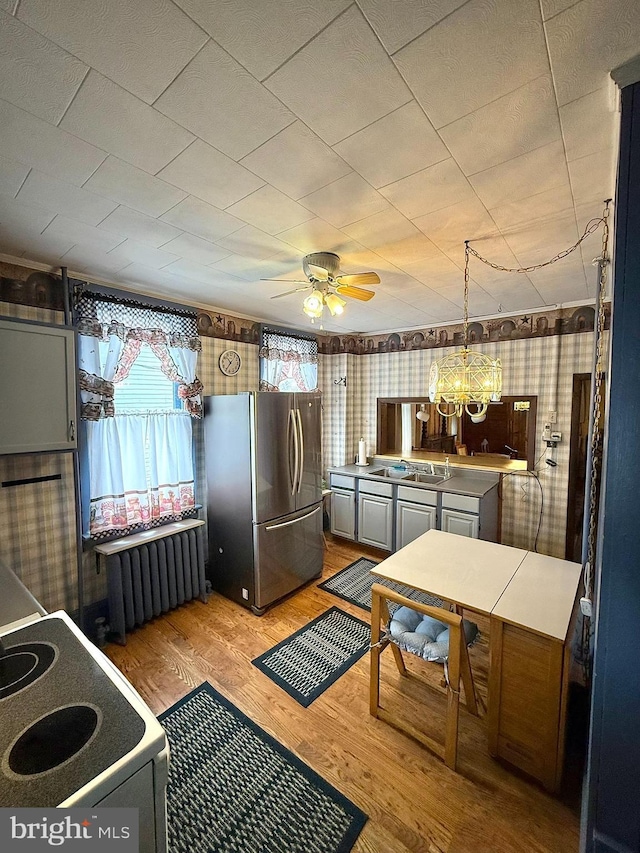 kitchen featuring white electric range oven, light wood finished floors, radiator, freestanding refrigerator, and ceiling fan with notable chandelier