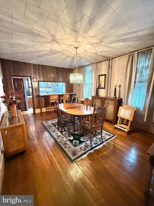 dining space with an inviting chandelier, wooden walls, and hardwood / wood-style floors