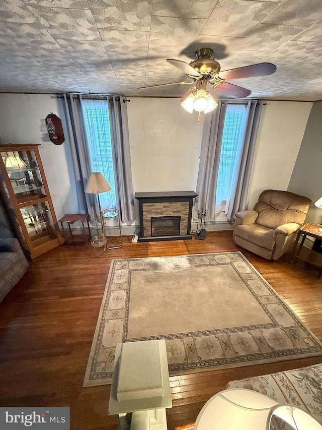 unfurnished living room with a ceiling fan, a healthy amount of sunlight, a stone fireplace, and wood finished floors