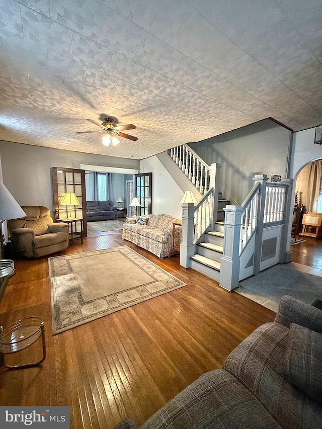 living room with a ceiling fan, arched walkways, wood-type flooring, and stairway