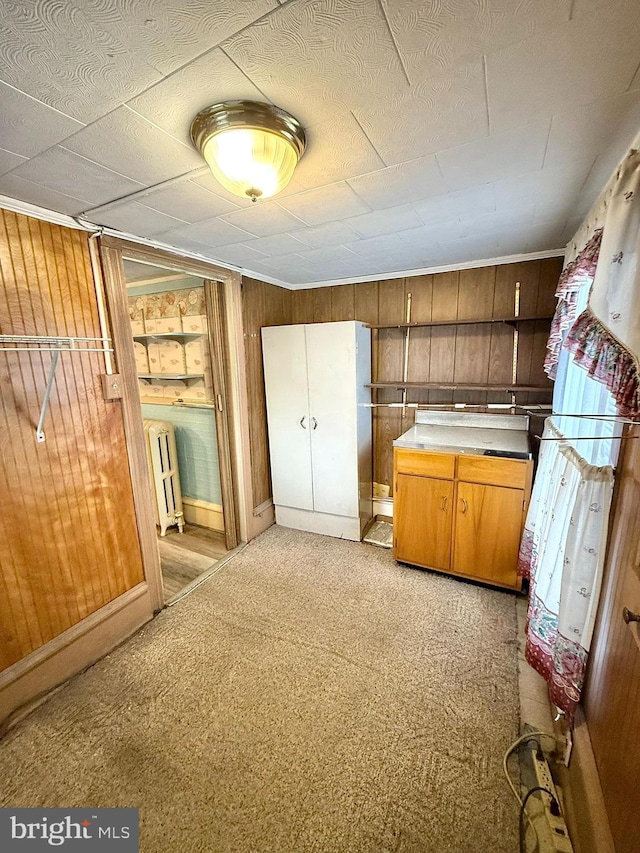 kitchen with brown cabinetry, radiator, light carpet, and wooden walls