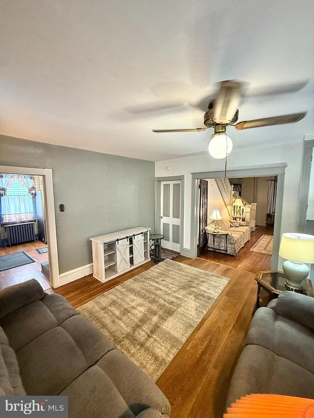 living area featuring radiator heating unit, wood finished floors, a ceiling fan, and baseboards