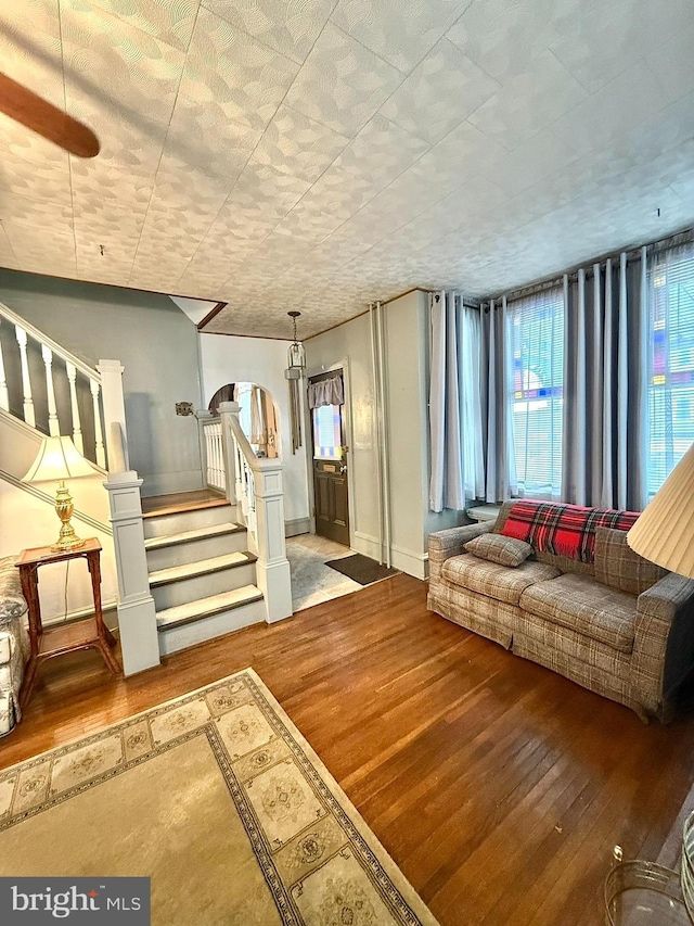 living area featuring arched walkways, stairway, baseboards, and wood finished floors