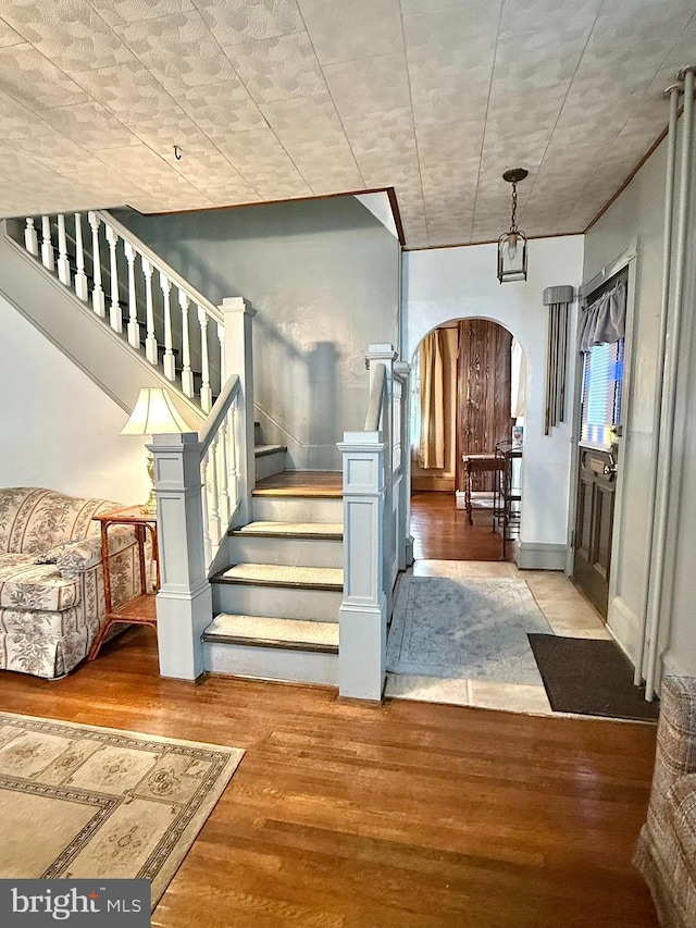 foyer entrance with arched walkways, stairway, baseboards, and wood finished floors