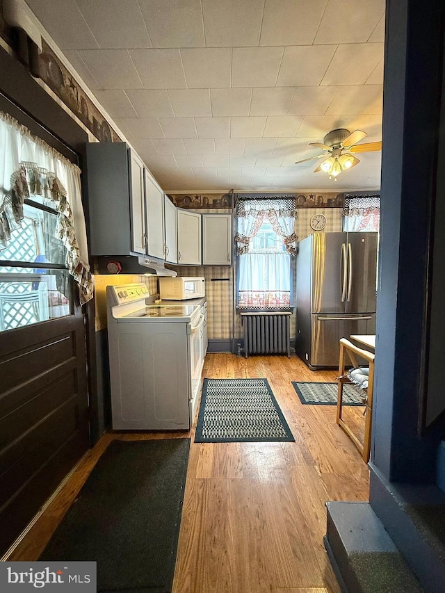 kitchen featuring washer / dryer, white microwave, light wood-style flooring, radiator heating unit, and freestanding refrigerator