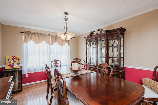 dining room with a textured ceiling, ornamental molding, and light wood-style floors