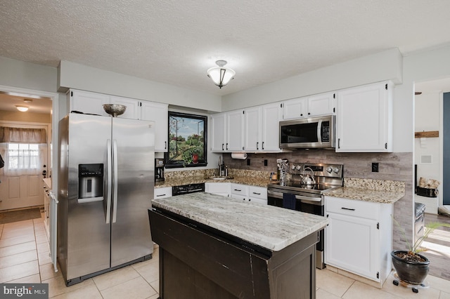 kitchen featuring light stone counters, stainless steel appliances, white cabinets, a center island, and tasteful backsplash