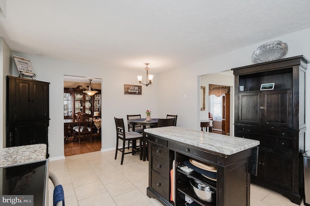 kitchen featuring light stone counters, decorative light fixtures, a notable chandelier, light tile patterned floors, and baseboards