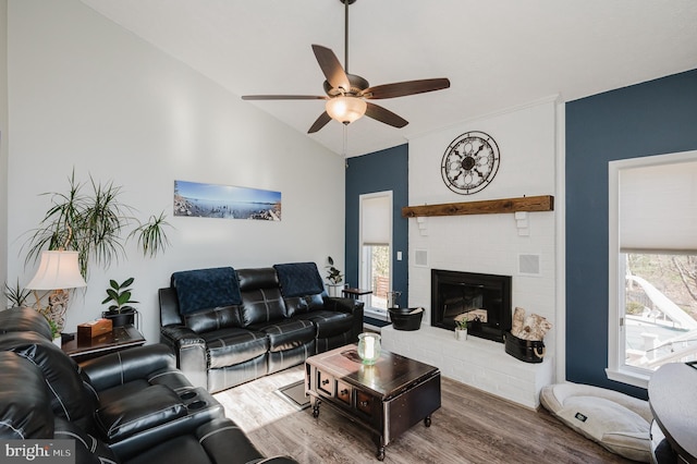 living area featuring lofted ceiling, a fireplace, a ceiling fan, and wood finished floors