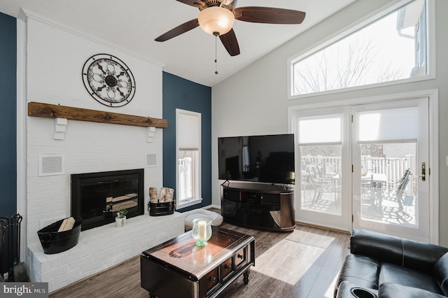 living area featuring lofted ceiling, ceiling fan, wood finished floors, visible vents, and a brick fireplace