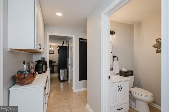 interior space with baseboards, toilet, tile patterned floors, an inviting chandelier, and vanity