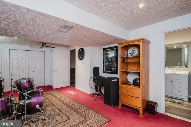 carpeted office space featuring baseboards, visible vents, a ceiling fan, a textured ceiling, and a sink