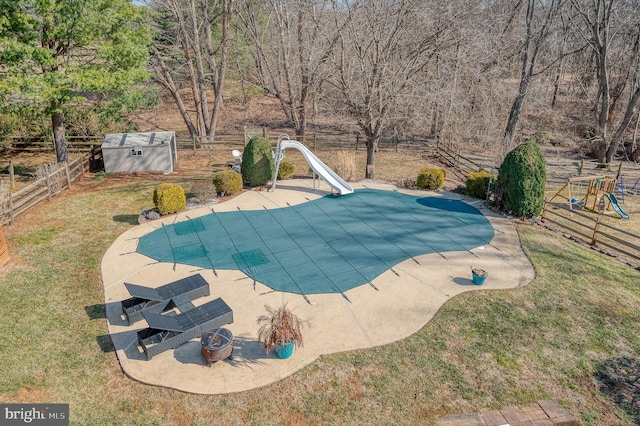 view of pool with an outbuilding, a covered pool, a storage shed, a water slide, and a fenced backyard