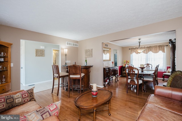 living area with light wood-type flooring, visible vents, a textured ceiling, and baseboards