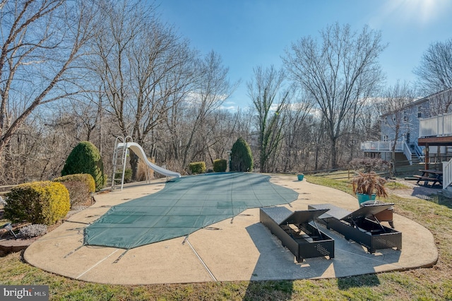 view of swimming pool featuring a patio, a water slide, and a covered pool