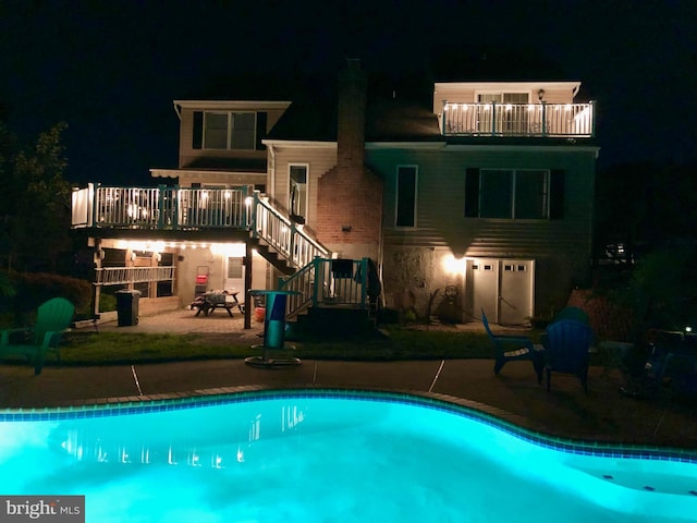 pool at twilight with a deck, an outdoor pool, a patio, and stairway