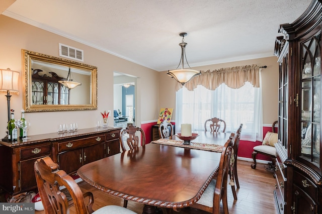 dining area featuring a textured ceiling, ornamental molding, wood finished floors, and visible vents