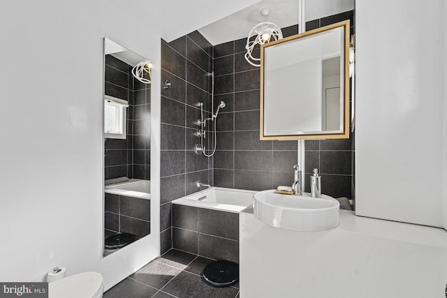 full bath featuring toilet, tile patterned floors, tiled shower / bath combo, a sink, and tile walls