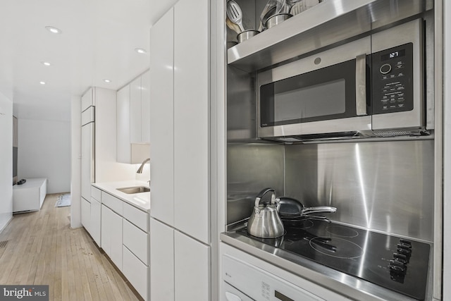 kitchen featuring a sink, light wood-style floors, white cabinets, stainless steel microwave, and modern cabinets