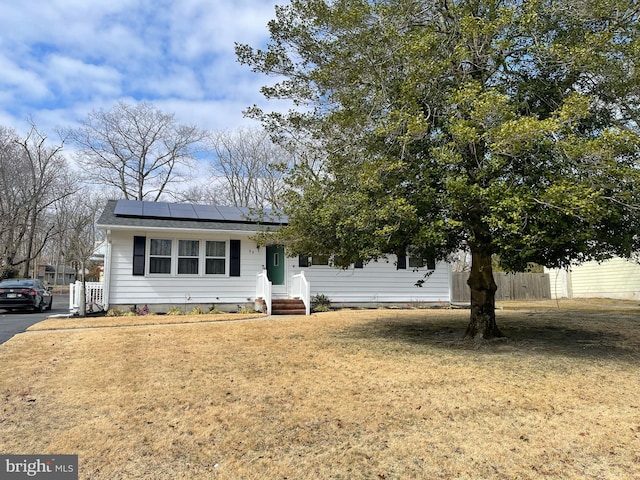 view of front of property with solar panels, a front yard, and fence