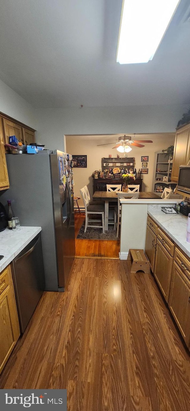 kitchen with stainless steel appliances, light countertops, brown cabinetry, dark wood-type flooring, and a ceiling fan