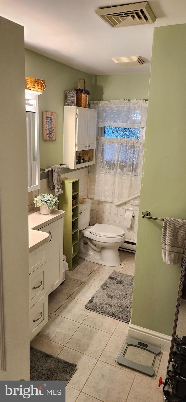 half bathroom featuring tile patterned flooring, toilet, a baseboard heating unit, vanity, and visible vents