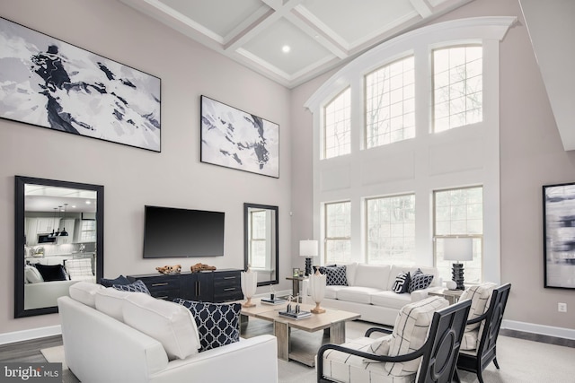 living area featuring coffered ceiling, wood finished floors, a towering ceiling, baseboards, and beamed ceiling