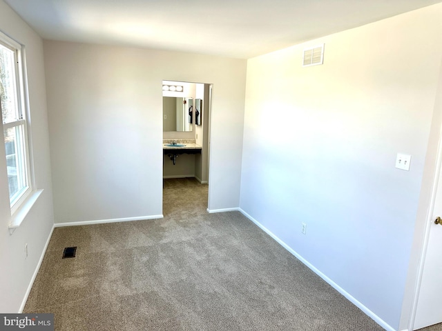 spare room featuring carpet floors, baseboards, visible vents, and a sink