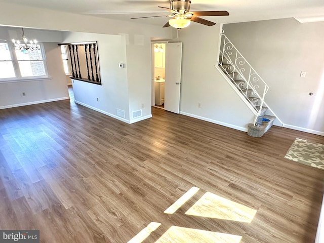 unfurnished living room featuring stairs, baseboards, wood finished floors, and ceiling fan with notable chandelier