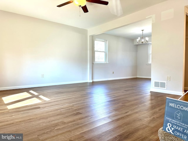 empty room featuring ceiling fan with notable chandelier, dark wood-style flooring, visible vents, and baseboards