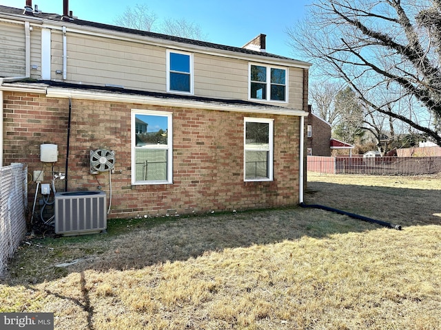 rear view of property with central AC, brick siding, a lawn, and fence