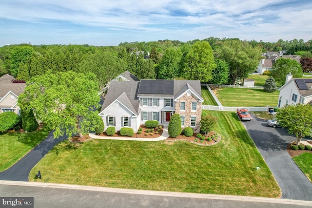 view of front facade with aphalt driveway, stone siding, fence, and solar panels