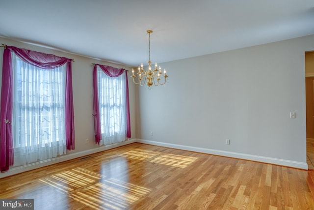 empty room featuring a chandelier, visible vents, light wood-style flooring, and baseboards