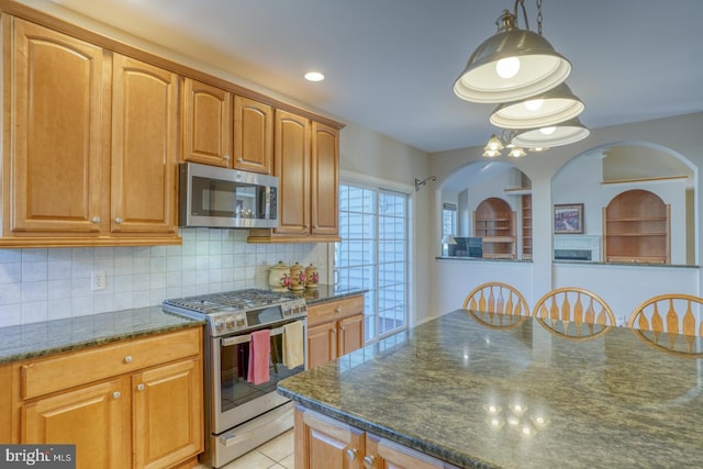 kitchen featuring decorative light fixtures, light tile patterned floors, stainless steel appliances, tasteful backsplash, and dark stone countertops