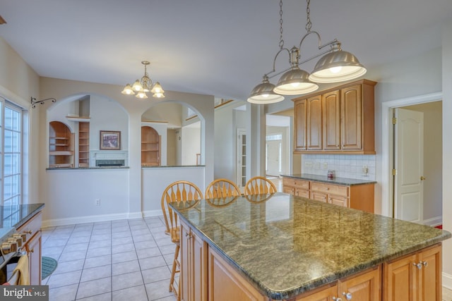 kitchen with tasteful backsplash, baseboards, brown cabinetry, a center island, and light tile patterned flooring