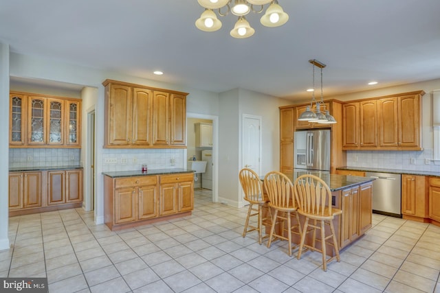 kitchen featuring light tile patterned floors, appliances with stainless steel finishes, a breakfast bar area, dark stone countertops, and a center island