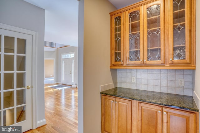 kitchen featuring light wood finished floors, glass insert cabinets, and backsplash