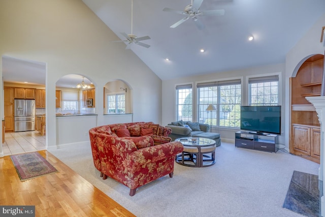 living area with baseboards, arched walkways, a ceiling fan, light colored carpet, and high vaulted ceiling