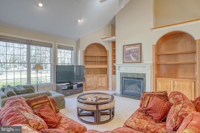 living room featuring high vaulted ceiling, built in shelves, a premium fireplace, and carpet floors