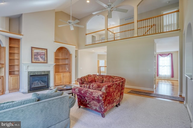 carpeted living area featuring built in features, a fireplace, visible vents, a ceiling fan, and baseboards