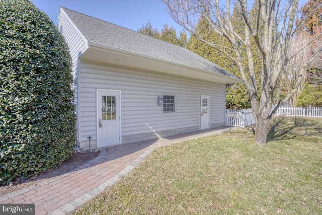 rear view of property with roof with shingles, fence, and a lawn