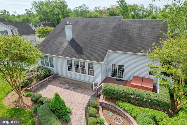 rear view of house with roof with shingles, a patio, and a chimney