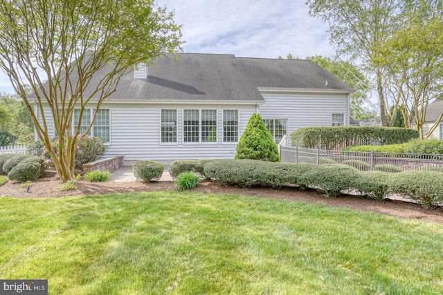 rear view of property featuring fence, a chimney, and a lawn