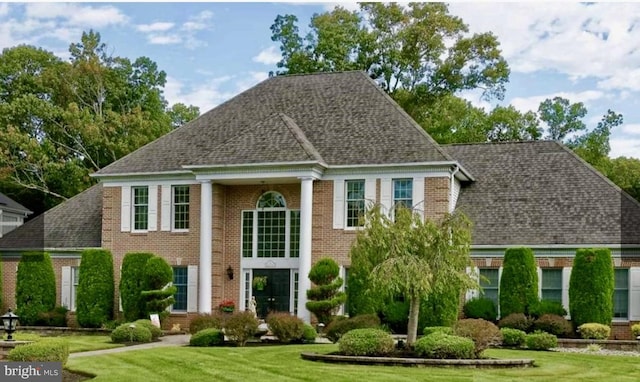 view of front facade with brick siding, a shingled roof, and a front yard