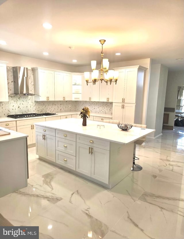 kitchen with marble finish floor, light countertops, a kitchen island, and wall chimney range hood