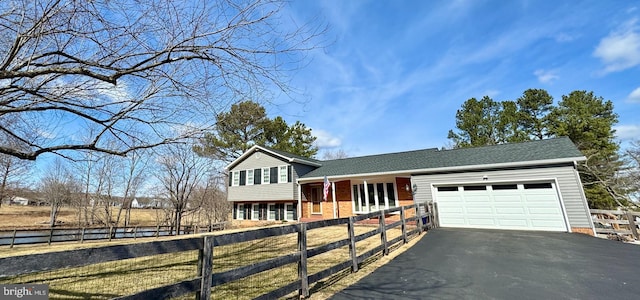 split level home with a garage, a fenced front yard, aphalt driveway, and brick siding